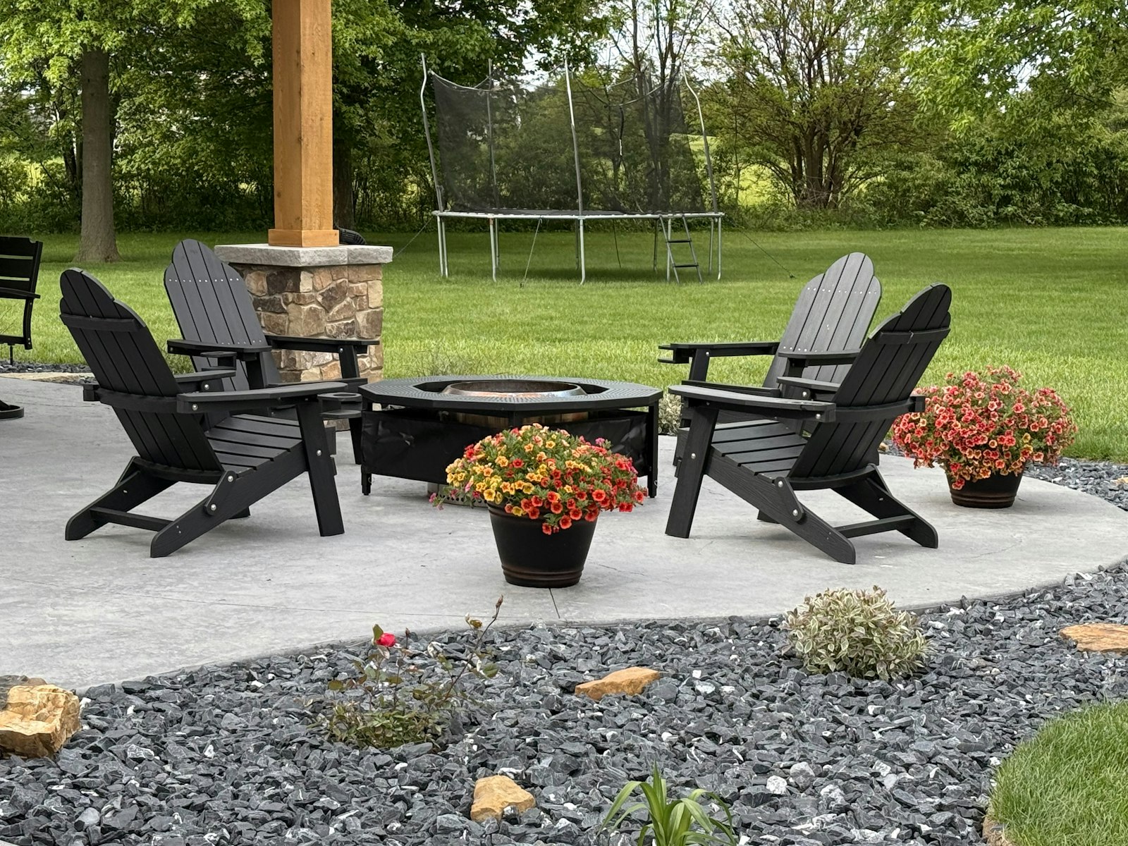 Stone fire pit surrounded by Adirondack chairs on a patio pad