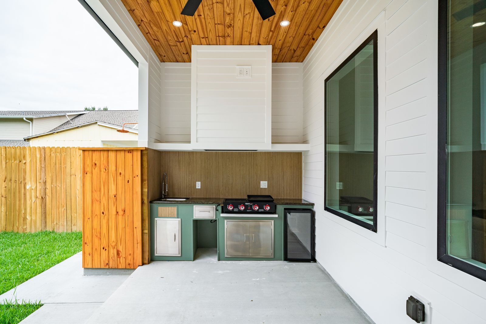 Built-in outdoor kitchen with a stainless grill and refrigerator under a covered patio