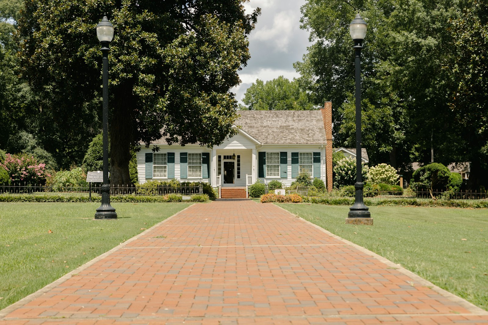 Wide paver walkway leading to a home front entry, lined with lamp posts and lawn